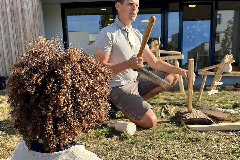 Ein Holzkünstler zeigt Kindergartenkindern, wie man den Werkstoff Holz bearbeitet.
