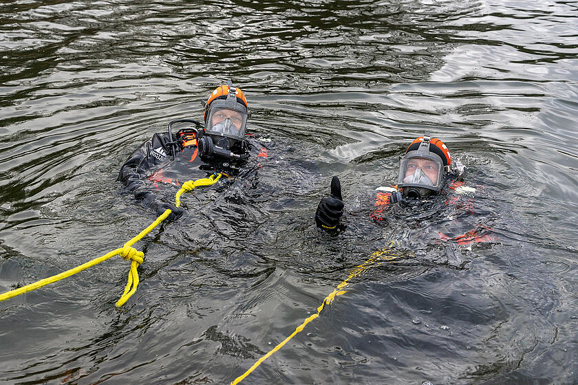 Zwei Taucher befinden sich im Wasser, einer von beiden macht eine Daumen-hoch-Geste.