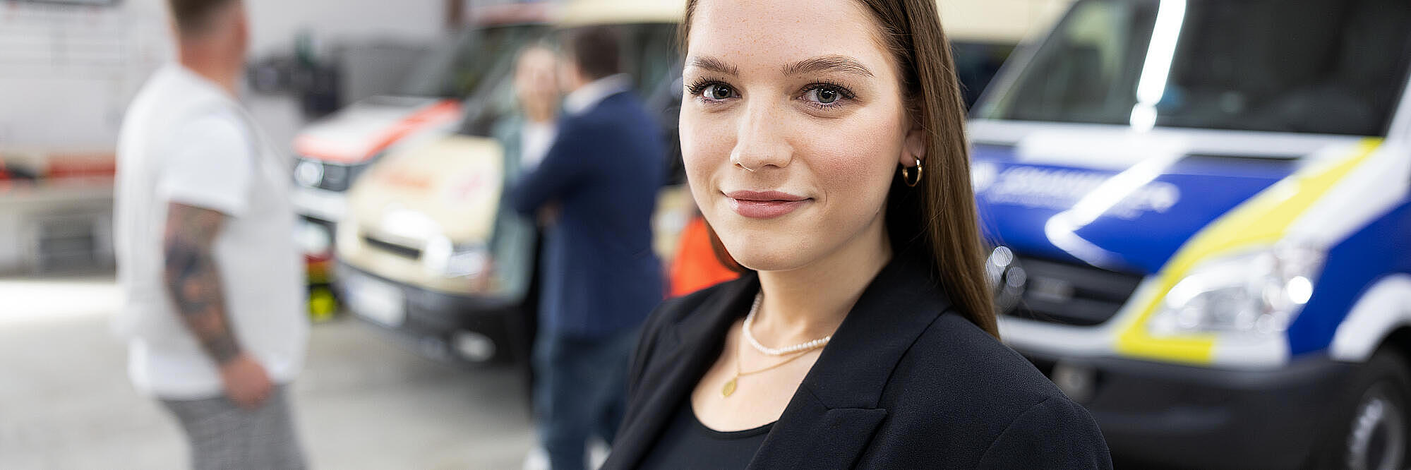 Junge Frau vor mehreren Rettungsfahrzeugen in einer Fahrzeughalle, Blick in die Kamera.