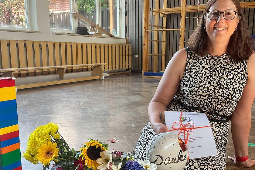 Eine Erzieherin sitzt auf dem Boden. Vor ihr stehen Blumensträuße und Geschenke.