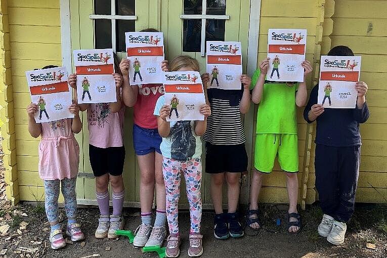 Sieben Kita-Kinder stehen mit ihren Urkunden stolz vor dem Spielehäuschen der Kita Ritternest.