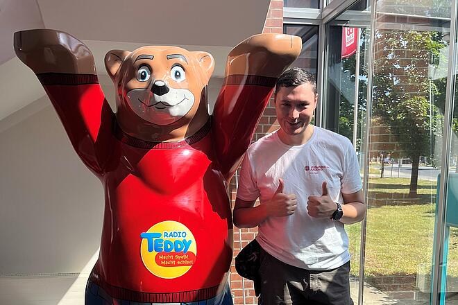 Ein Mitglied der Johanniter-Jugend posiert neben der Bärenfigur von Radio Teddy und gibt zwei Daumen hoch.