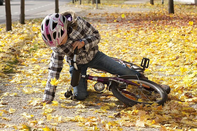 Ein Kind stürzt von seinem Fahrrad auf einem mit gelben Laub bedeckten Weg.
