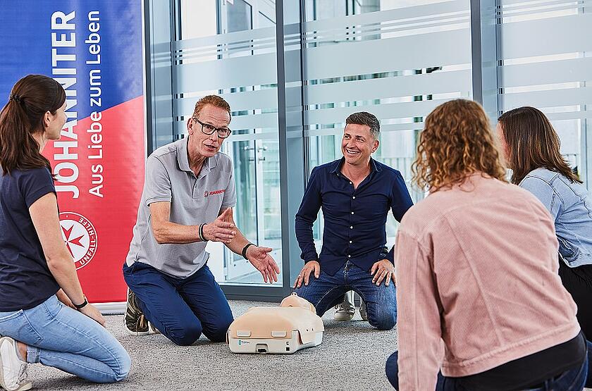 Ein Erste Hilfe Trainer erklärt den Teiknehmenden die Herz-Druck-Massage