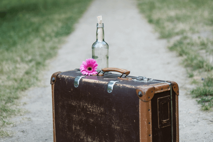 Koffer auf dem Weg mit Blume und Flaschenpost