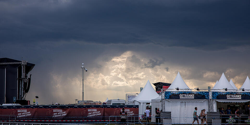 Festivalgelände mit Verkaufszelten und Bühnen vor dunklen Gewitterwolken