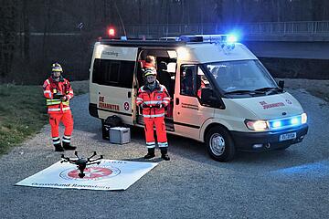 Ehrenamtliche Mitglieder einer Johanniter-Drohnenstaffel mit ihrer Drohne vor einem Einsatzfahrzeug.