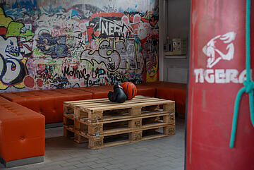 Ein Fitnessraum mit roter Sitzecke und einem Tisch aus Paletten.
