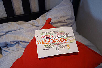 Schild mit "Herzlich willkommen" auf einem Bett