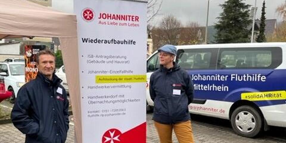 Zwei Mitarbeitende vor einem Roll-up der Johanniter-Fluthilfe