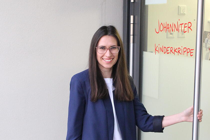 Eine Frau öffnet die Tür zu einer Johanniter Kinderkrippe und lächelt in die Kamera.