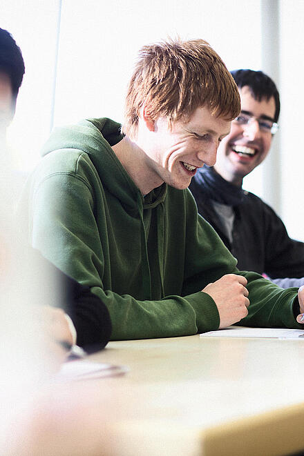 Studierende sitzen im Klassenraum und schreiben, unscharfer Vordergrund.