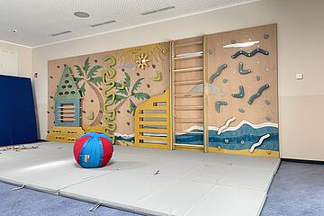 Ein Raum mit Turnmatten, einem Ball und einer Kletterwand.