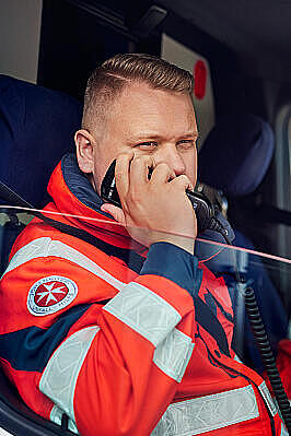 Ein Johanniter sitzt im Rettungswagen, das Fenster ist offen und er setzt einen Funkspruch ab