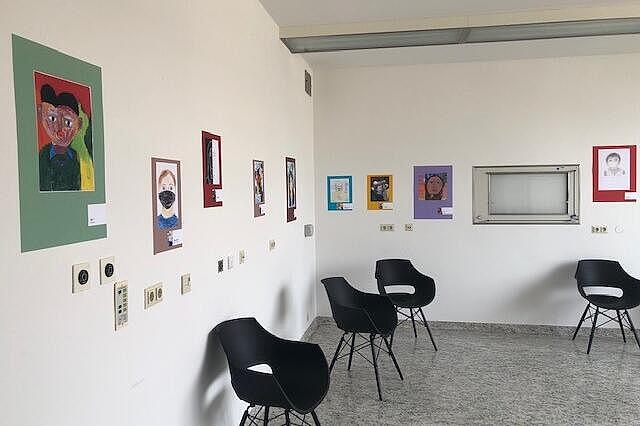 Heller Raum mit Stühlen und an der Wand aufgehängten Bildern, eingerichtet als kleiner Ausstellungsbereich.