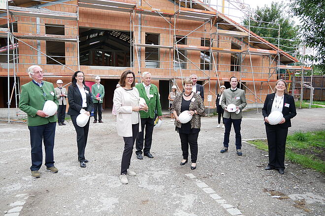Mehrere Leute stehen vor einem Haus das gerade im Bau ist und tragen Johanniter Helme.