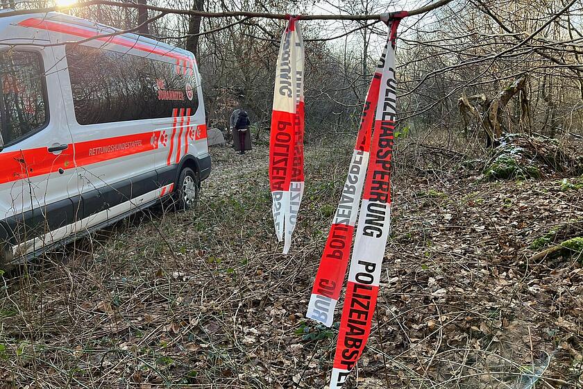 In einem Waldstück steht ein Johanniter-Transporter, daneben ist ein Absperrband zu sehen.