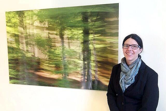 Eine Frau steht vor einem großen Bild eines Waldes, das an einer Wand hängt.