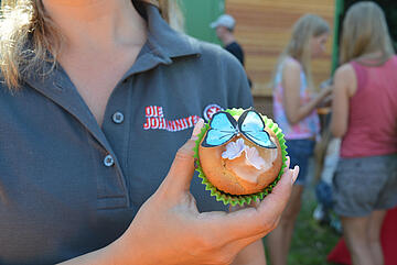 Ein bunt verzierter Cupcake wird in die Kamera gehalten