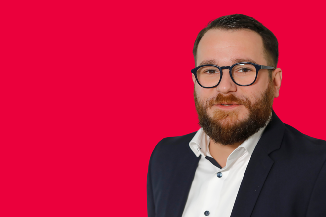 Portrait eines Mitarbeiters vor rotem Hintergrund