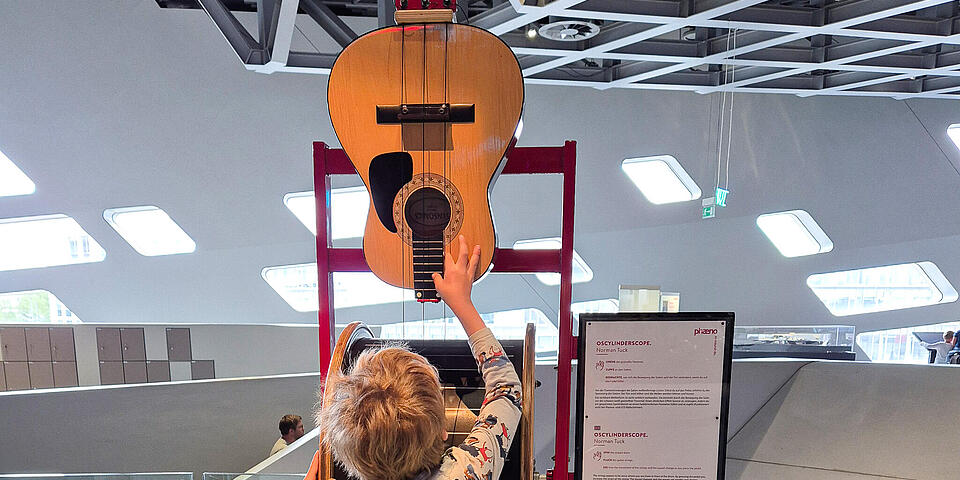 Eine Gitarre ohne Hals verkehrt herum aufgehängt. Ein kind fasst sie an.